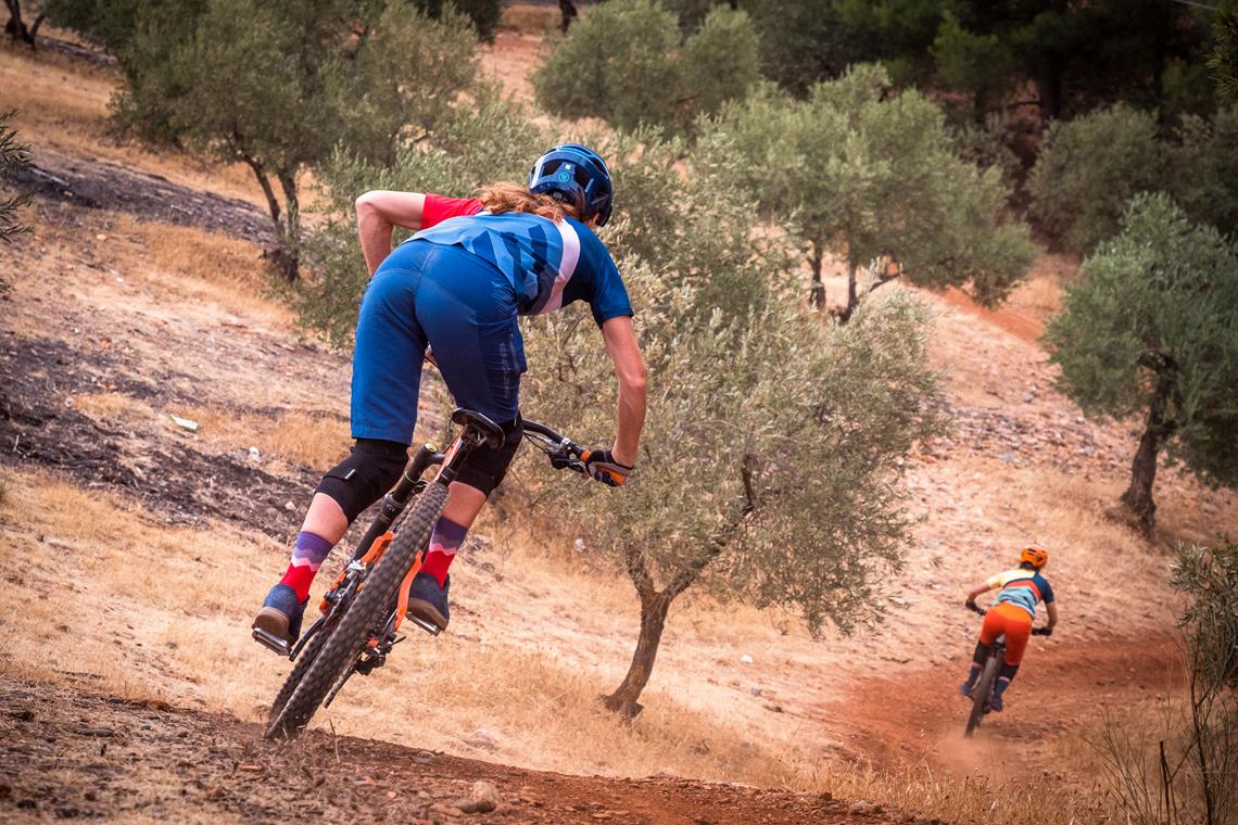 Para rowerzystów zjeżdża szlakiem górskim w śródziemnomorskim anturażu.