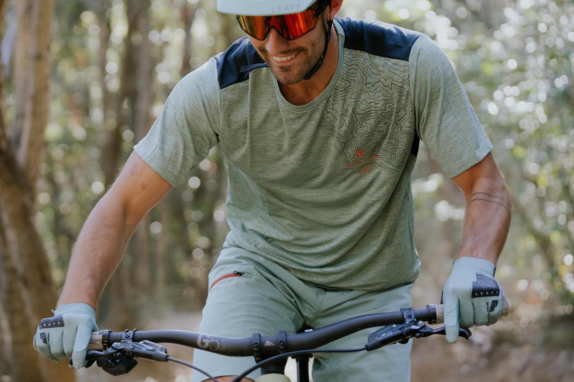 Mężczyzna jedzie rowerem górskim w szarym stroju marki Leatt.